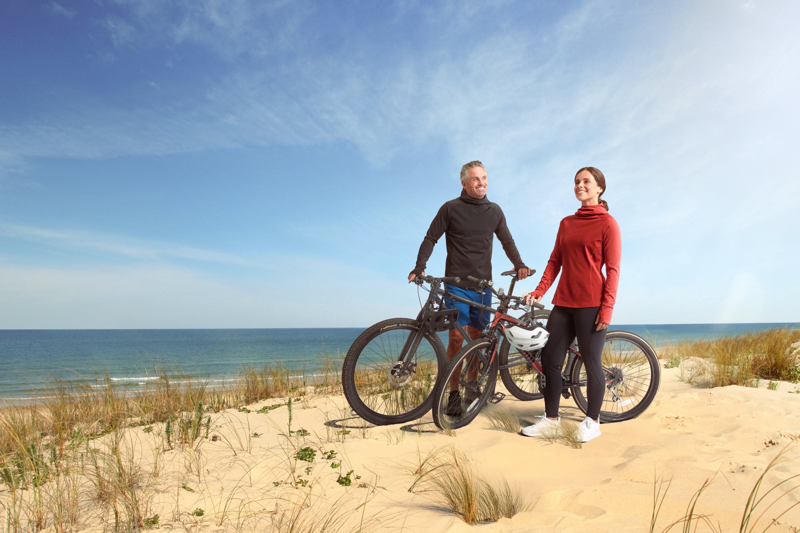 Paar mit Fahrrädern in den Dünen, sie in UVEEKAI UV-Leggings